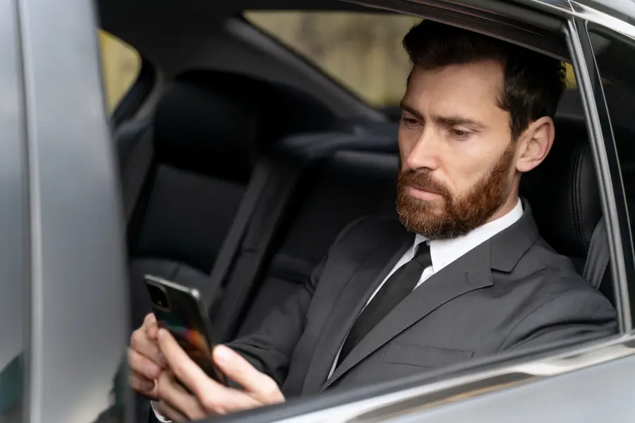 Smartphone affichant une réservation de transport devant une voiture avec chauffeur